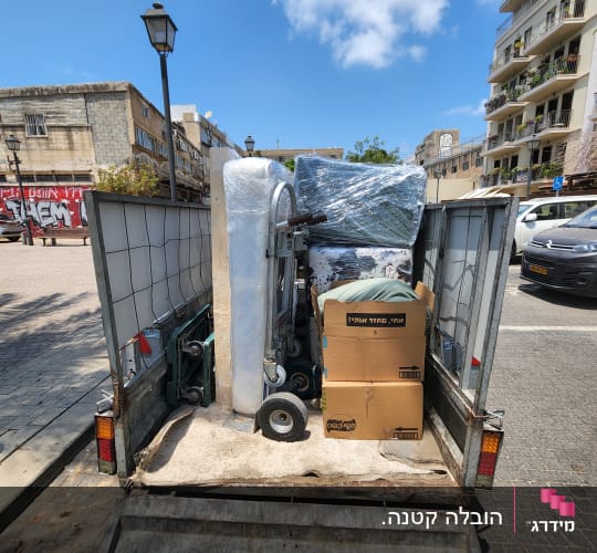 משאית עם ציוד ארוז, קרטונים ומזרן ברחוב עירוני
